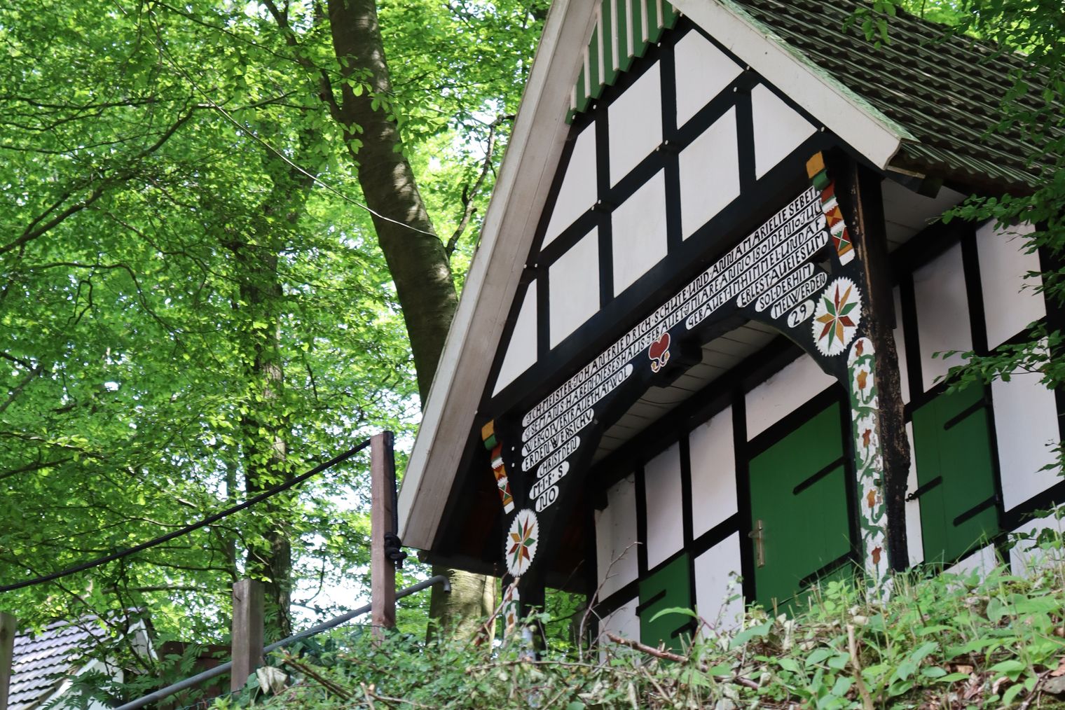 Fachwerkhäuschen im Wald, umgeben von grünem Laub, auf einem Hügel gelegen, malerische Szene.