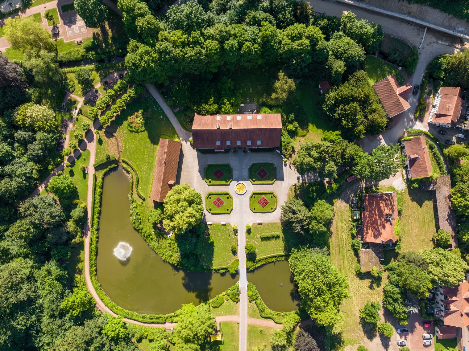 Luftaufnahme einer historischen Parkanlage mit symmetrischen Gärten, Teich und zentralem Gebäude.