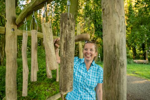 Frau in kariertem Hemd spielt auf hängenden Holzinstrumenten entlang eines Waldlehrpfads.