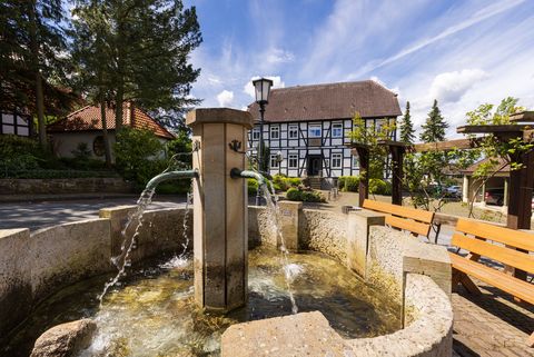 Historischer Fachwerkhof in Levern mit Brunnen im Vordergrund und blauen Himmel im Hintergrund.