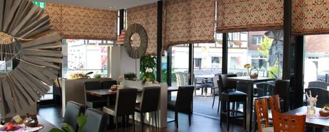 Helles Café mit stilvollen Vorhängen, gemütlichem Mobiliar und Aussicht auf eine Sonnenterrasse.