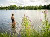 Eine Person im Badeanzug steht im klaren Wasser eines Sees, umgeben von grüner Natur.